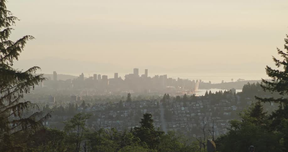 Downtown Vancouver skyline is seen through layers of trees from a distance at sunset