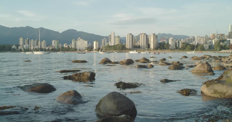 Ripples flow around stores on shore with mist covered city and mountains in background
