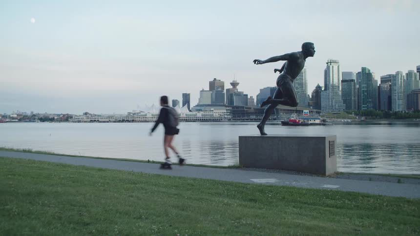 A woman roller skates on a path along the waterfront across from downtown Vancouver