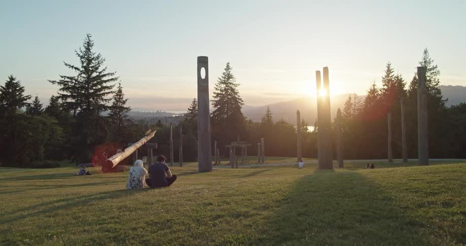 People sitting on the grass in Burnaby Mountain Park at sunset