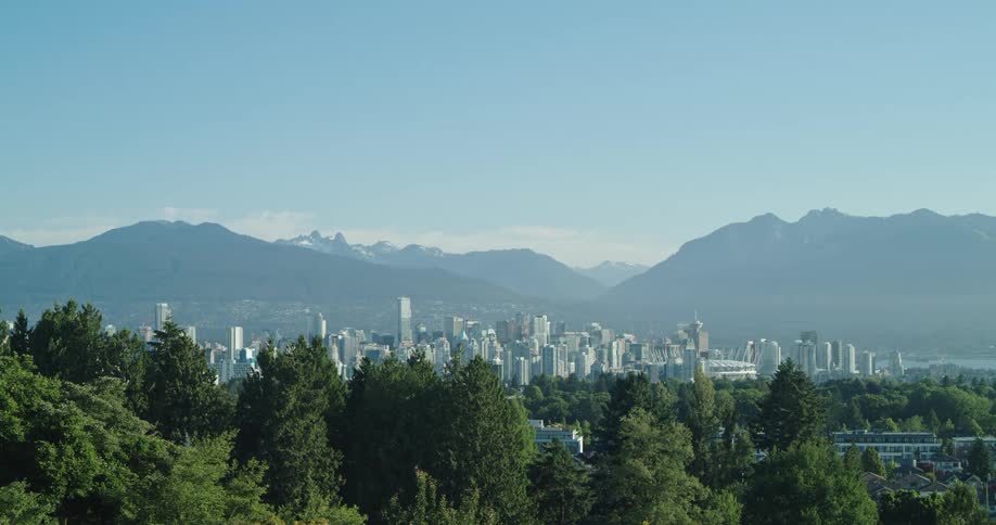 Downtown Vancouver is seen through the trees on a sunny day with North Shore mountains in the background