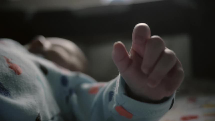 A baby lays on the floor waving its hand
