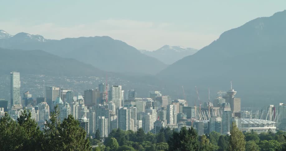 A city skyline with buildings with a mountain range the sky and clouds in the background