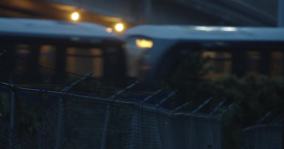A train travels past a bridge and a barbed wire fence
