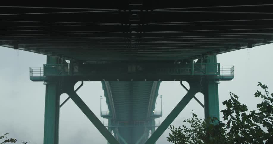 The underside of an enormous bridge can be seen as it is shrouded in fog