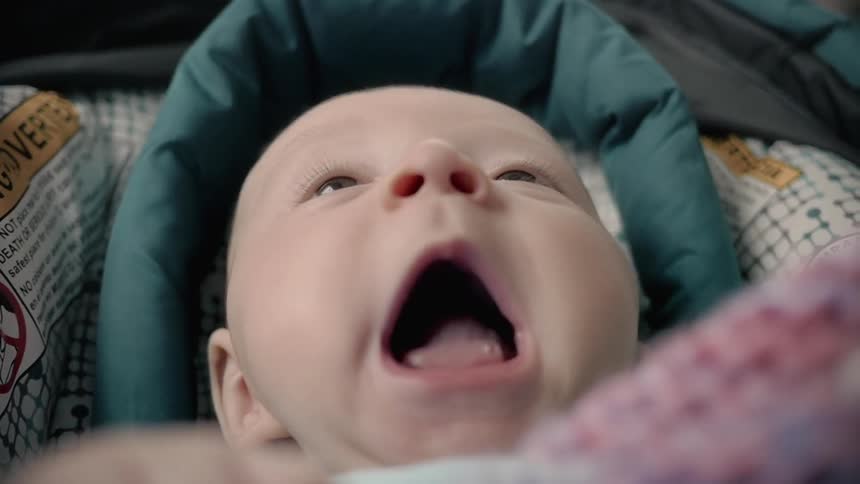 A baby laying in a car seat yawns