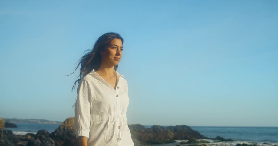 A woman smiles and poses as she walks on a rocky coast