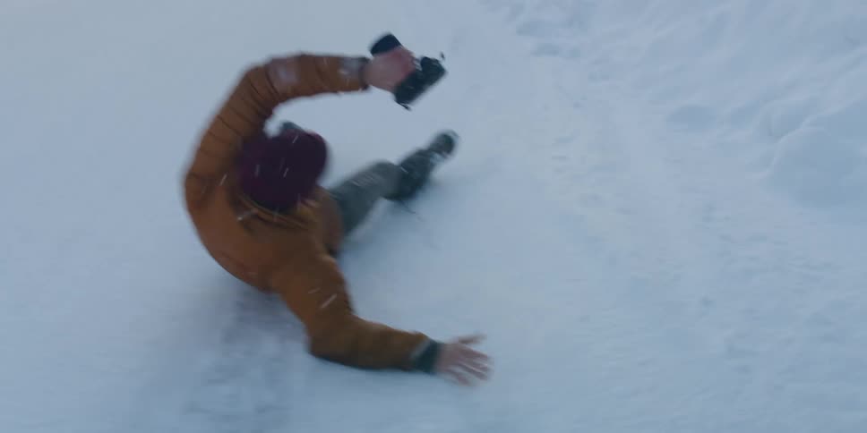 A photographer laughs after falling while running through snow toward a forest