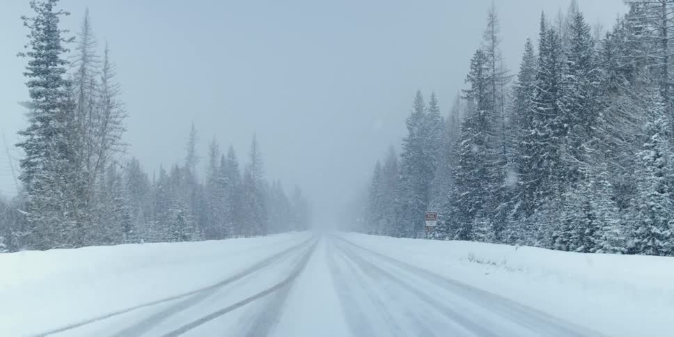 A road covered in snow with trees the sky and clouds in the background