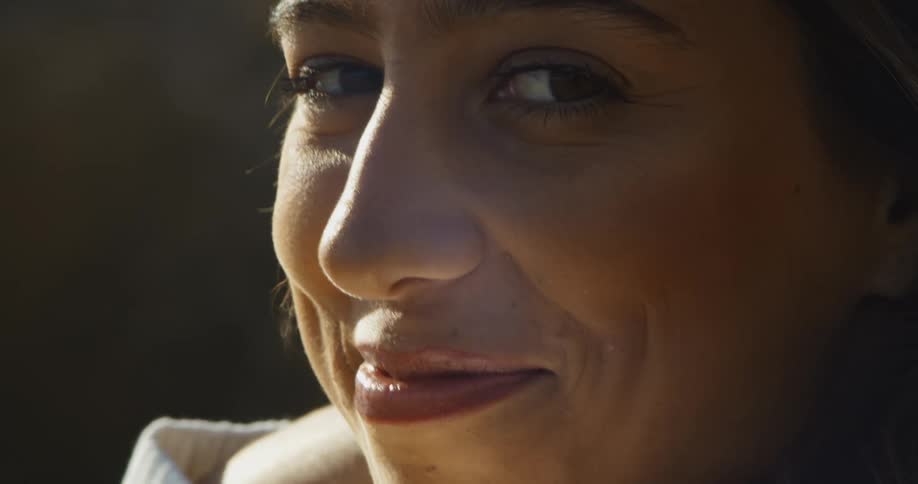 A woman relaxing outdoors turns to smile into the camera