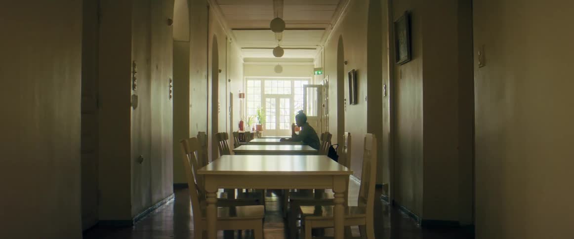 A student studies at a middle table of tables that fill a long narrow room in a library