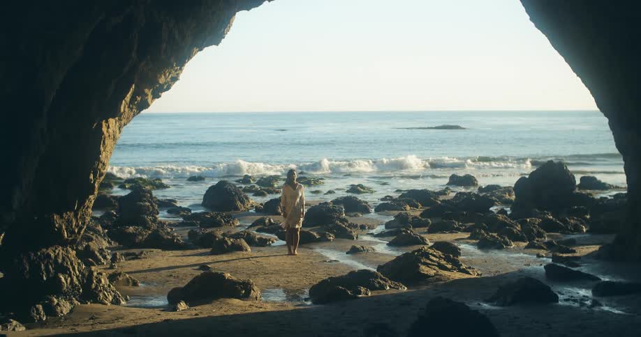 A woman is standing at the coast of a beach