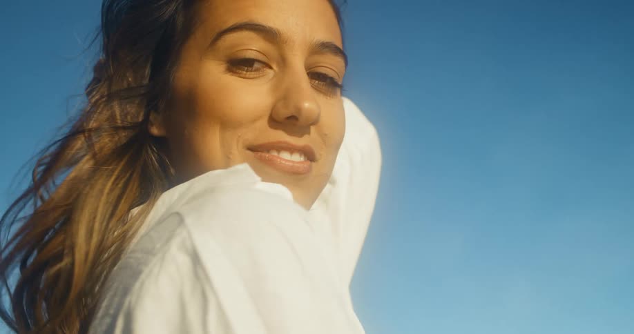 A woman smiling and staring with the sky and clouds in the background