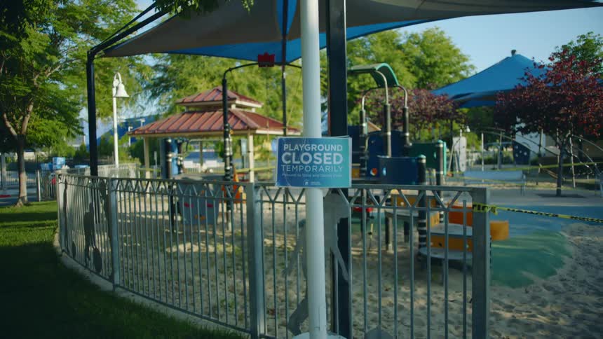 A closed sign posted outside a public playground on a sunny day