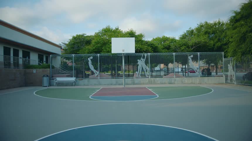 A playground with a basketball court with trees the sky and clouds in the background