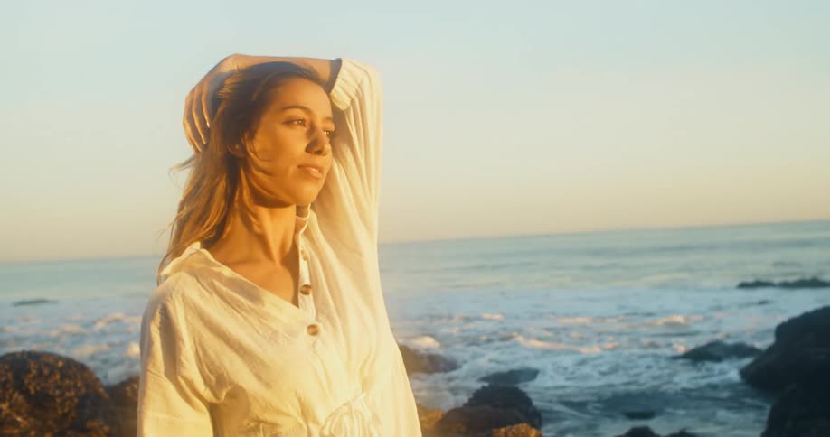 A woman standing on a rocky shore with the ocean the sky and clouds in the background