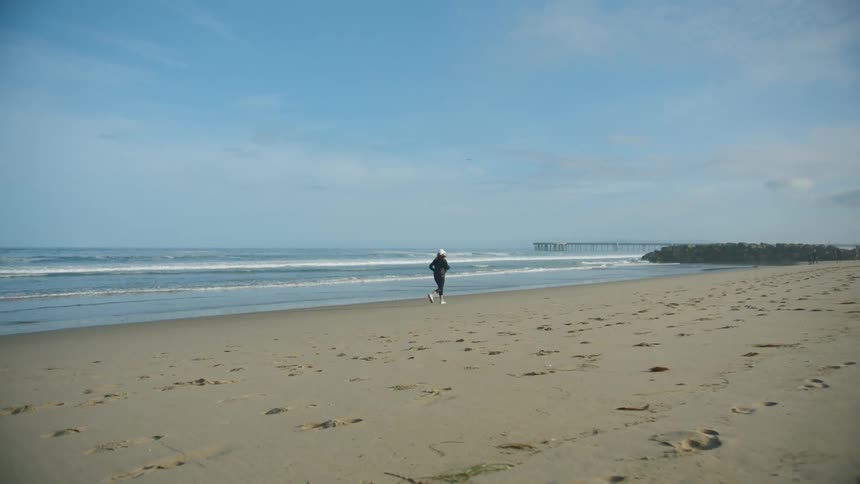 A woman jogs along a beach on a clear day