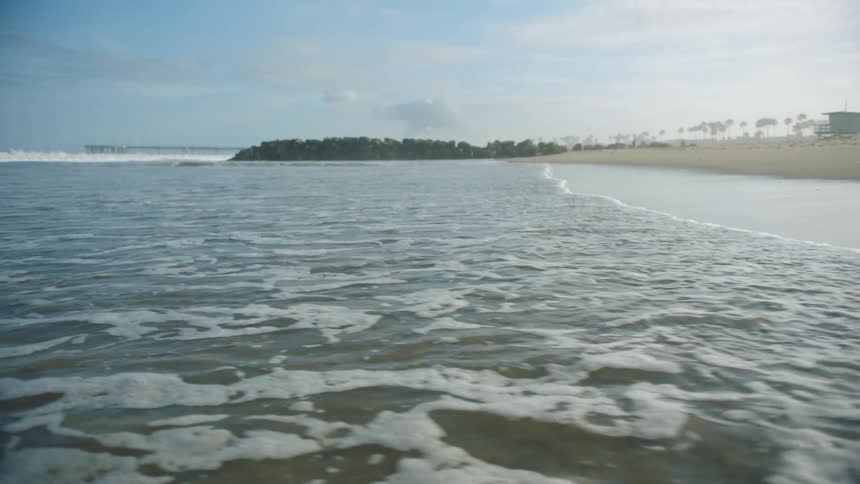 The tide washes into a sandy beach on a sunny day