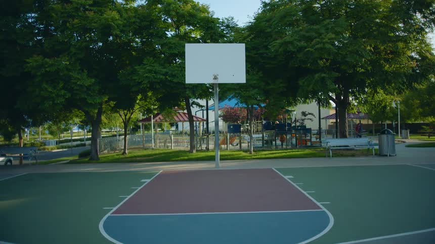 An empty basketball court with a playground behind on a sunny day