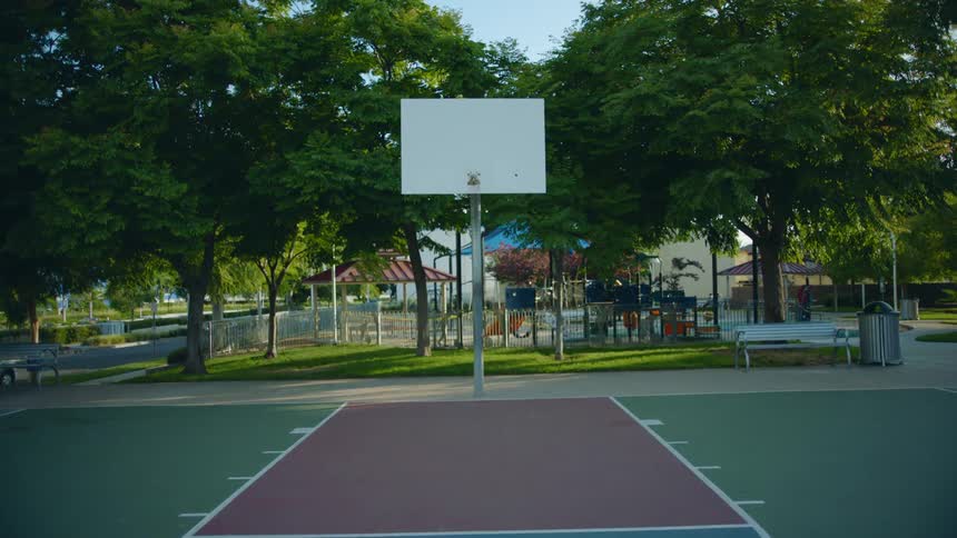 An empty basketball court with a backboard without a net and a playground behind