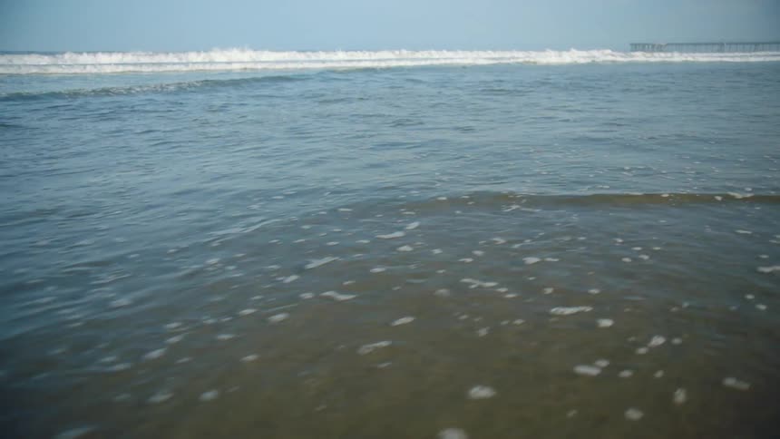 Ocean waves wash into a sandy beach on a clear day