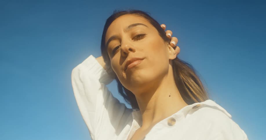 Woman stands outdoors reaching hand over her hair under clear deep blue sky