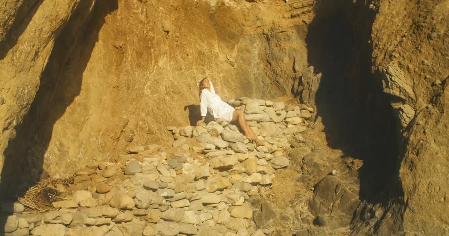 A woman poses for a photograph atop a pile of rocks beneath a cliff outdoors during the day