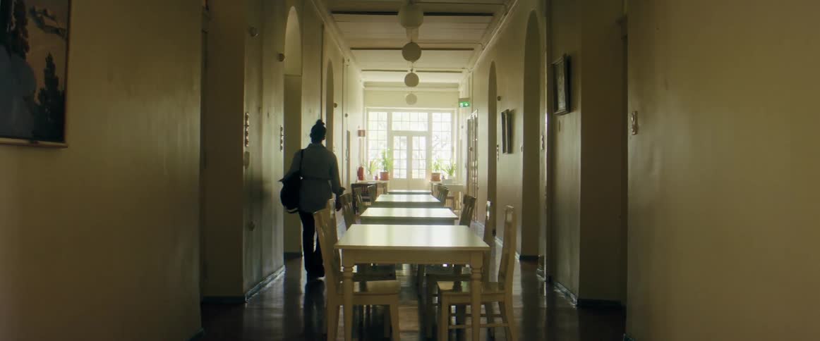 A woman walks through a long corridor filled with a row of dining tables