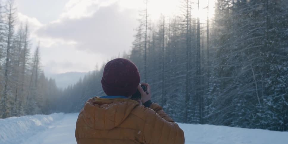 A man stands on a snowy path and takes a photo of the forest
