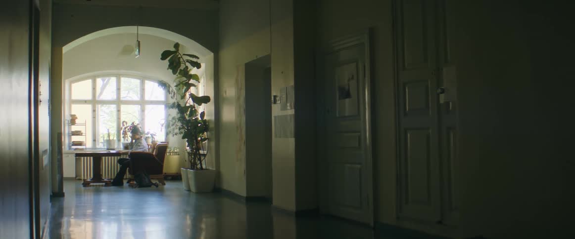 A woman studies while sitting at a desk in front of a large window at the end of a hallway