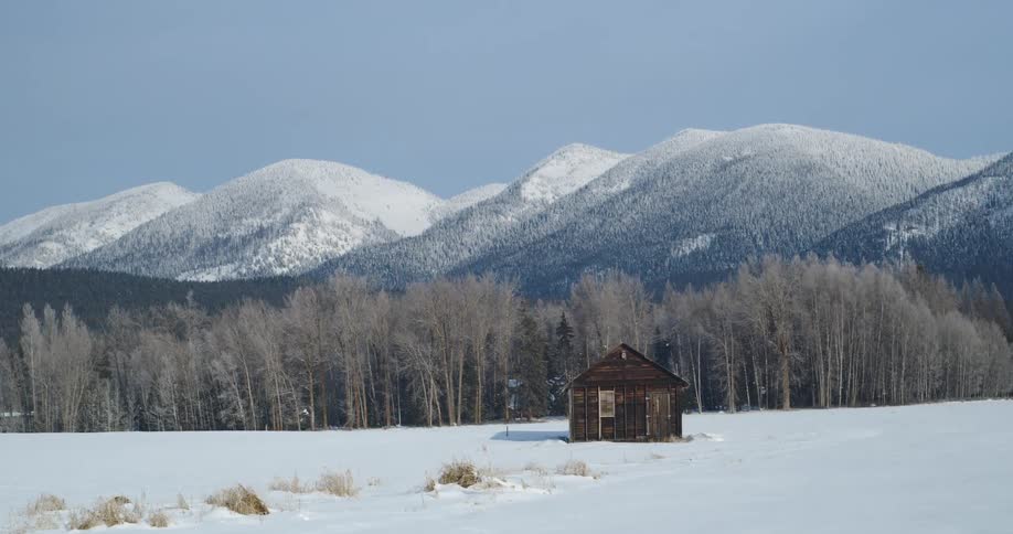 A cabin on a snowy field with trees a mountain range the sky and clouds in the background