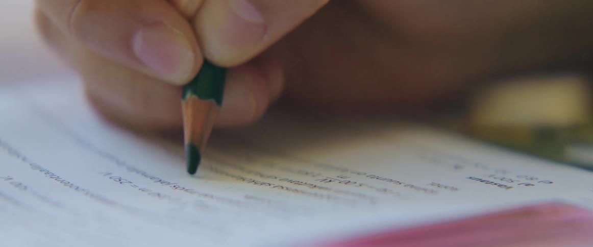 A person is filling out a worksheet using a wooden pencil