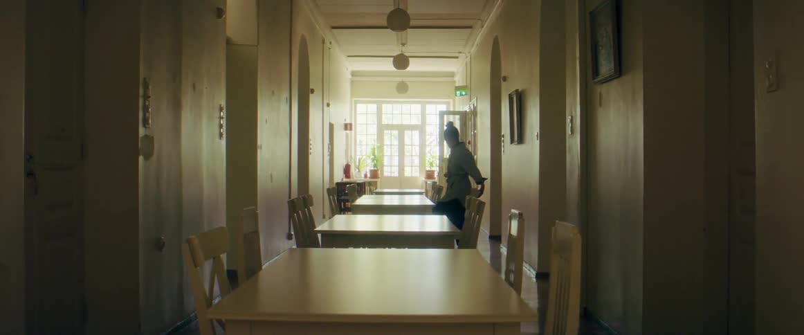 A young woman carrying a backpack walks around a table to take a seat on the other side