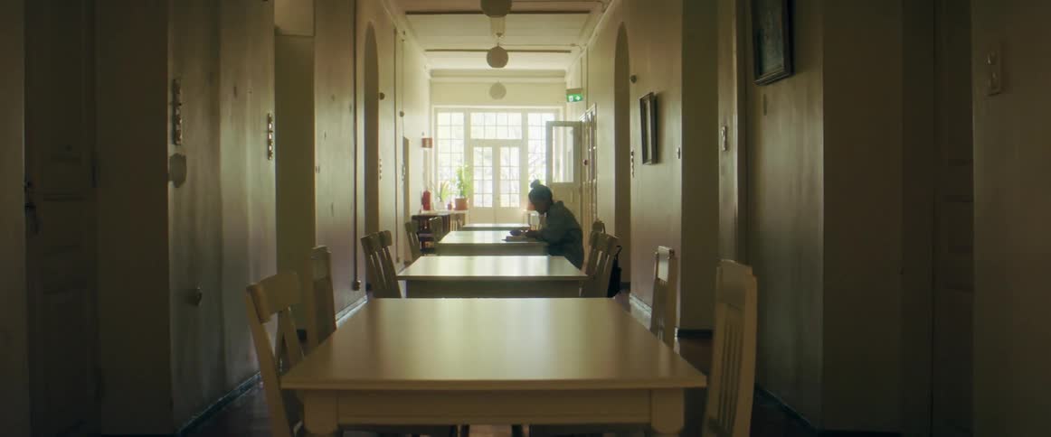 The silhouette of a woman sitting at a table in a long narrow space flipping pages studying and writing