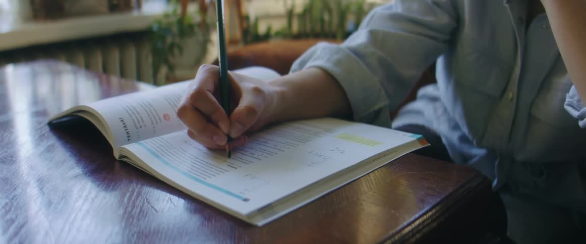 An adult sits at a table and fills out an answer to a question in a workbook