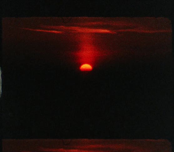 Sunrise sits in crimson red sky while darkness covers land