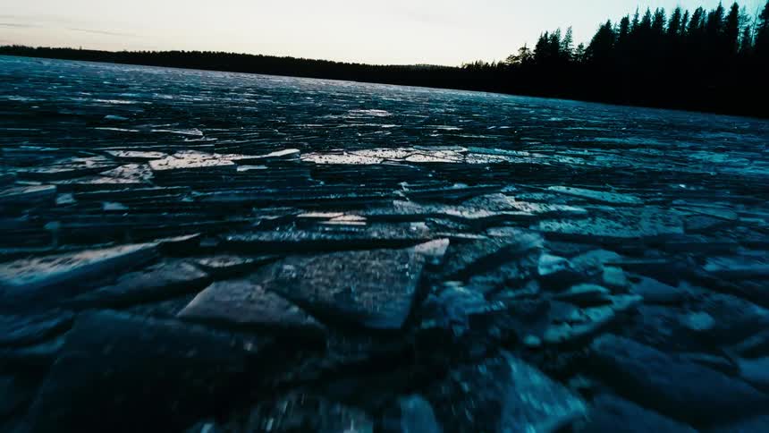 A frozen lake with ice with trees the sky and clouds in the background