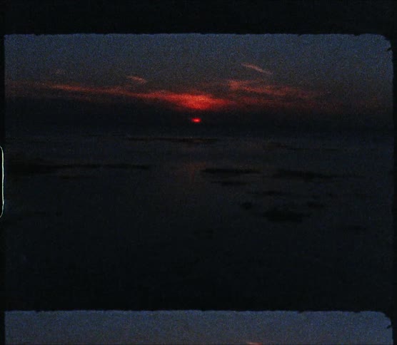 A body of water with land with a sunset the sky and clouds in the background
