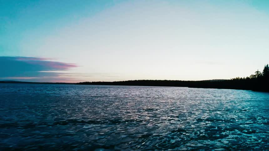 Pink tinted sky shines over conifer forest sitting on shore near ice covered water