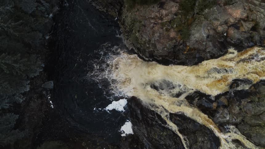 The yellow waters of a waterfall flows down a cliff into the river below