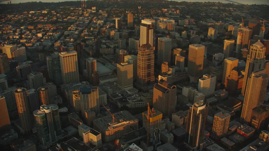 Sun casts shadows across downtown skyscrapers as river curves around city on misty day