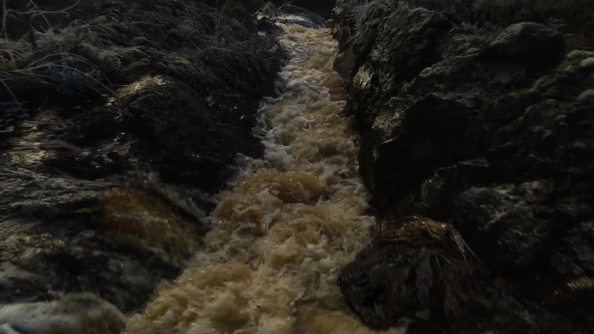 Muddy river water flows through a narrow channel then down a waterfall towards a canyon