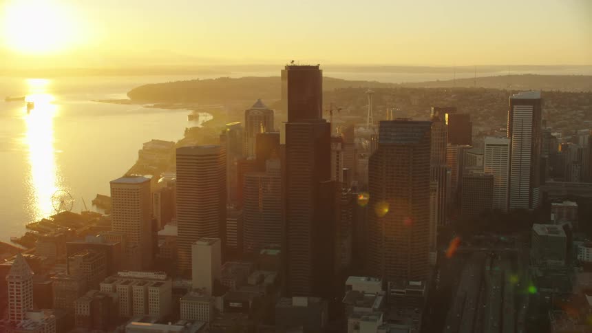Sun sits above the horizon on hazy day shining across water through city downtown
