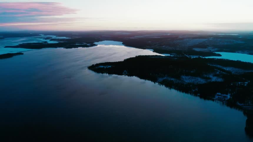 Snow covered roads and trees line the land surrounding lakes at dawn