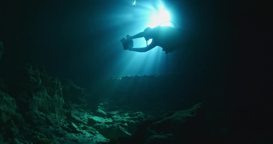 A man is scuba diving holding a camera in dark waters
