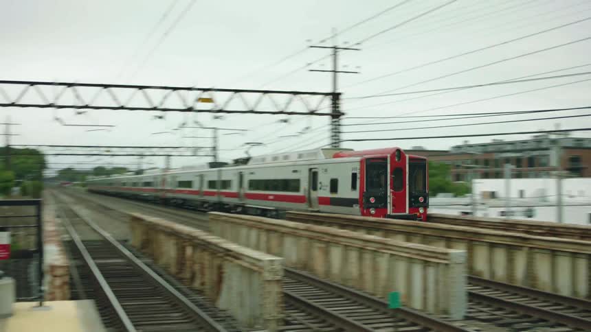 A train riding on a track with buildings trees the sky and clouds in the background
