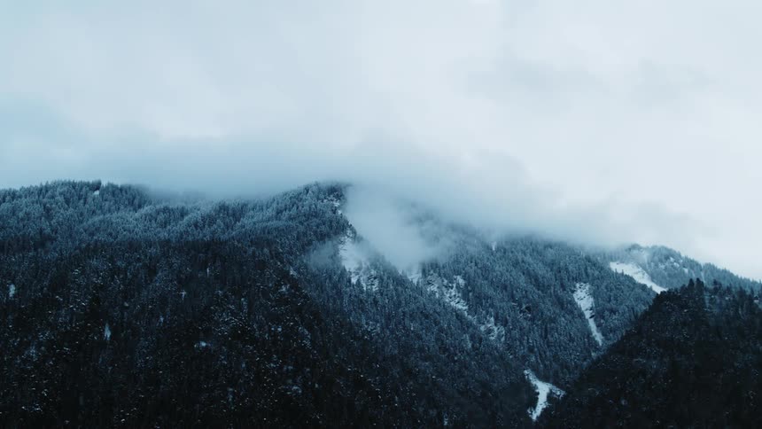 Low lying clouds obscure top of snow and ice covered forest occupying mountain near valley
