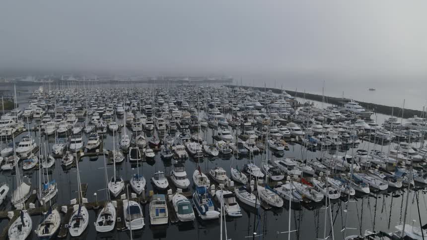 Slow orbit over the masts of sailboats and yatchs docked at a fog shrouded marina