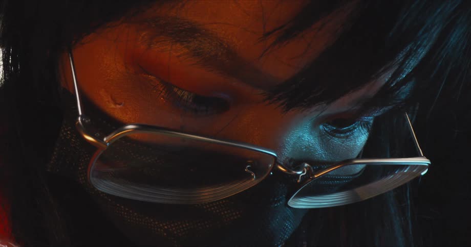 Asian person wearing eye glasses and a mask looks downward