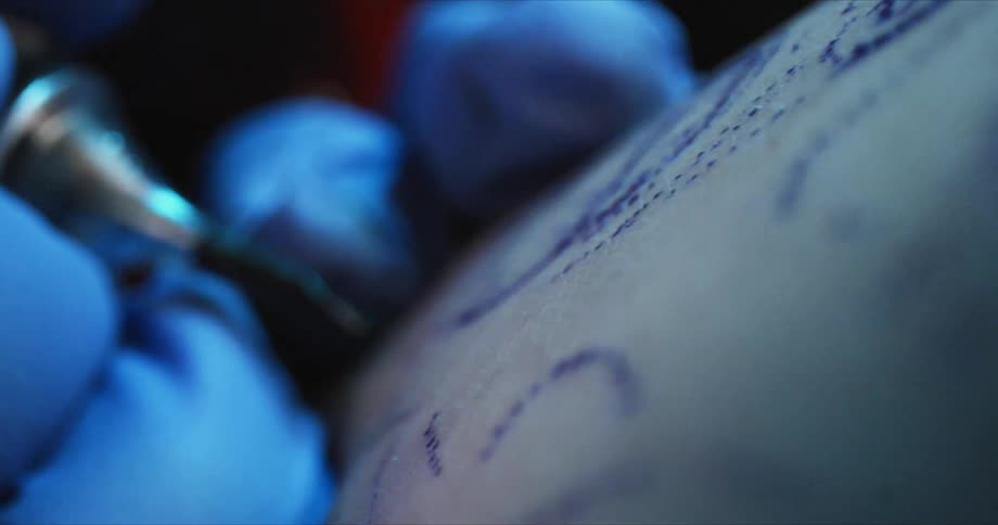 A person with a tattoo gun and gloves tattooing someones skin